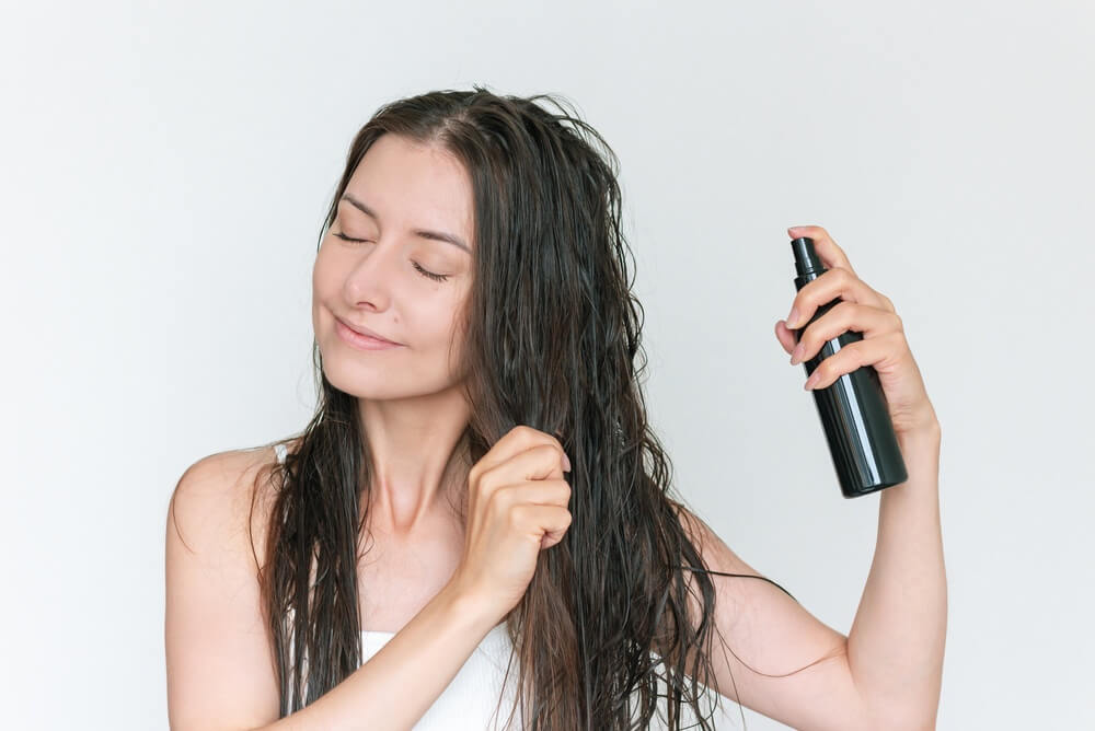 devojka stavlja keratin u spreju za negu kose