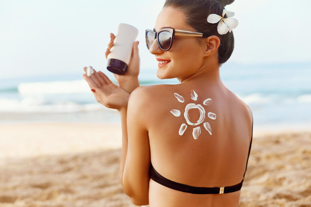 devojka nanosi kremu za sunčanje do sedi na plaži