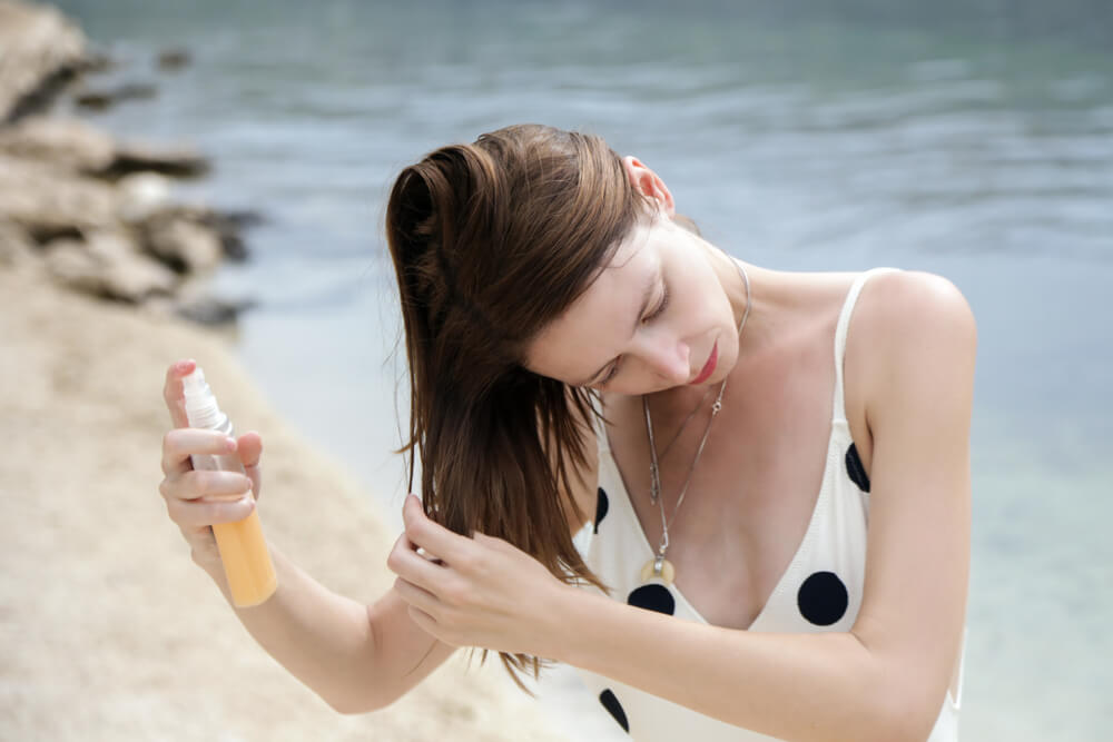 devojka na plaži nanosi preparat za negovanje kose