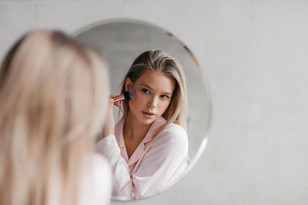 devojka nanosi bronzer na lice