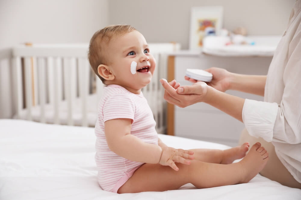 mama nanosi kremu za lice za bebe svojoj srećnoj bebi