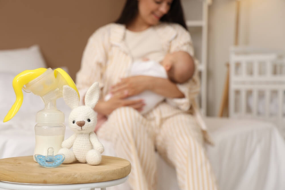pumpica za dojenje sa cuclom i igračkom na stolu dok mama doji dete u pozadini